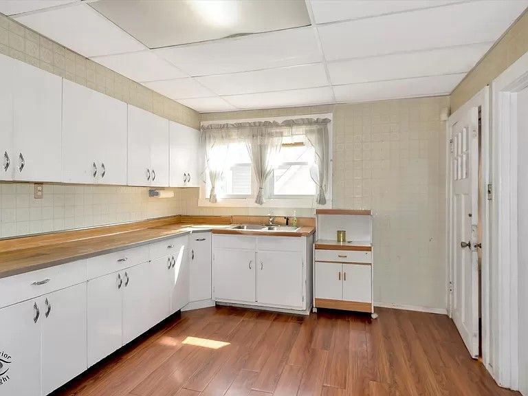 An empty kitchen with white cabinets and hardwood floors