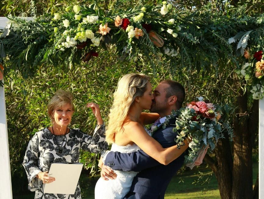 A Bride and Groom Are Kissing Under a Floral Arch — Vivienne Celebrant - Gold Coast Wedding Celebrant in Mudgeeraba, QLD