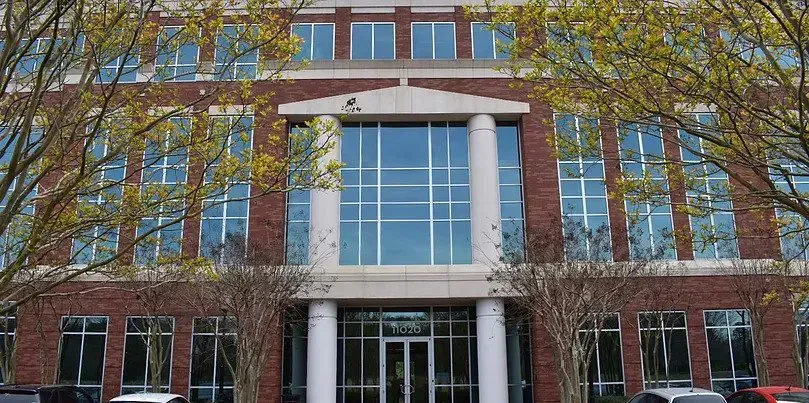 Boardroom with leather chairs, papers, and a coffee cup on a wooden table. A screen hangs on the wall.