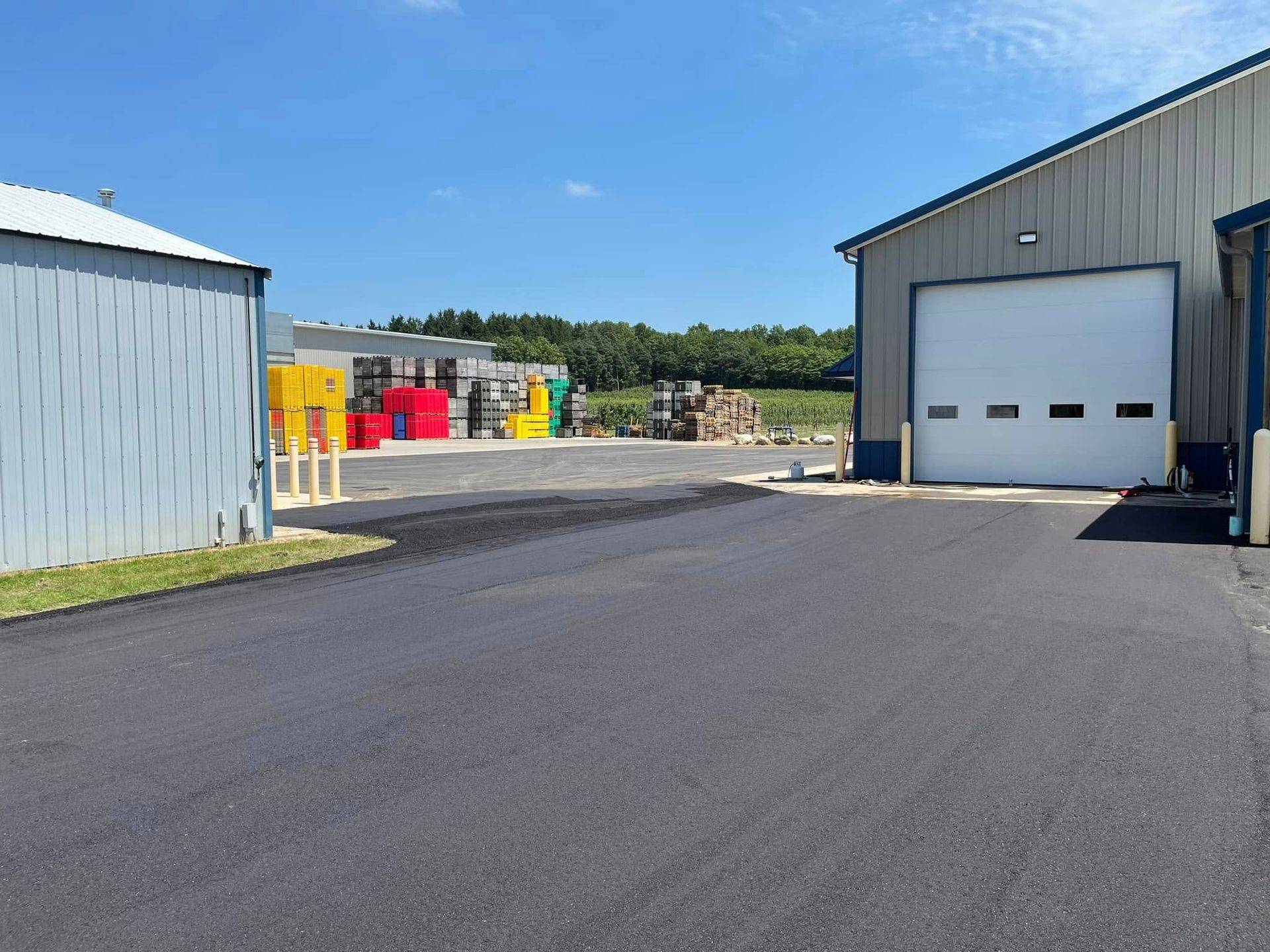 Industrial yard with a paved lot, metal buildings, and colorful equipment under a clear blue sky