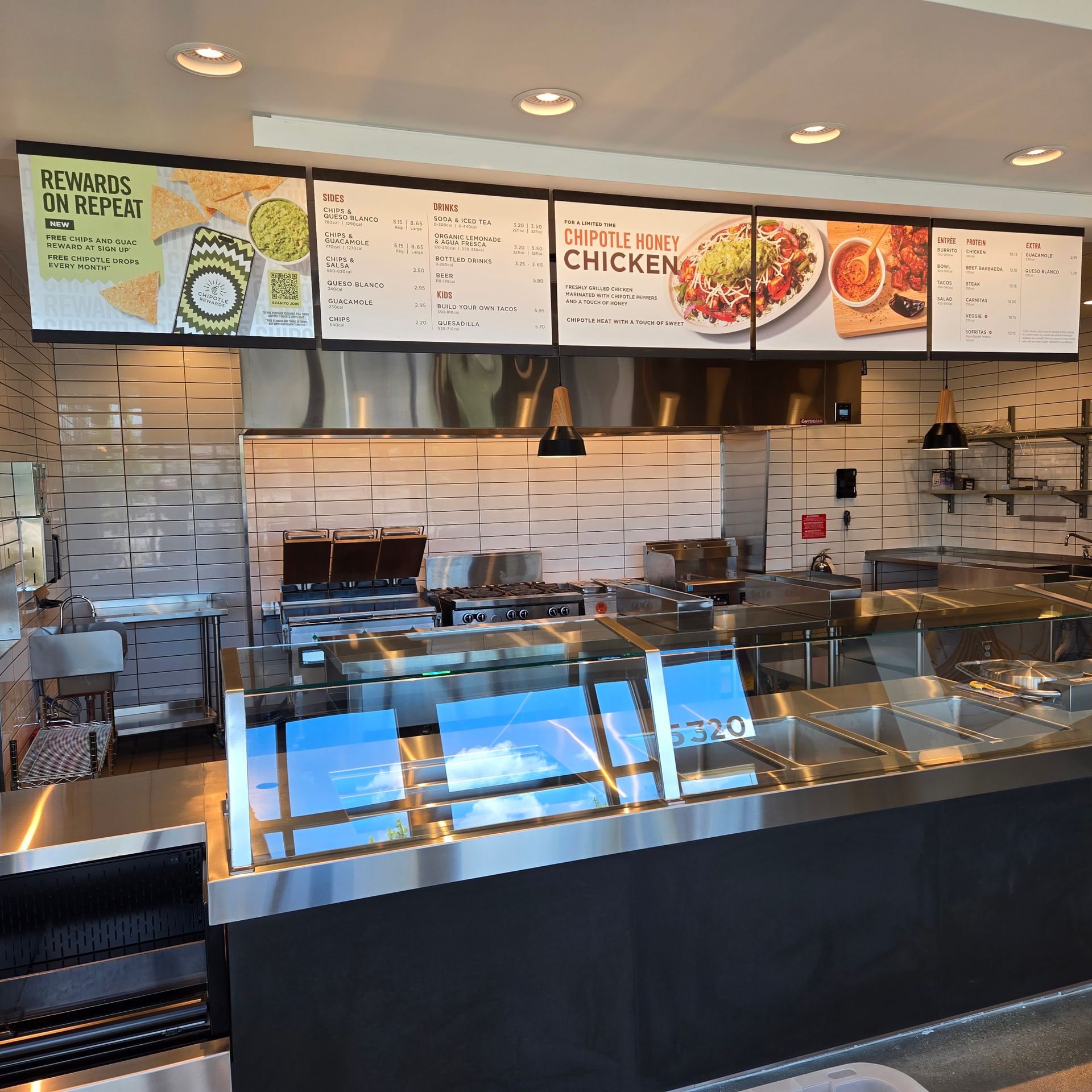 Fast-casual restaurant counter with menu boards, sandwich ingredients, and display case under bright lights