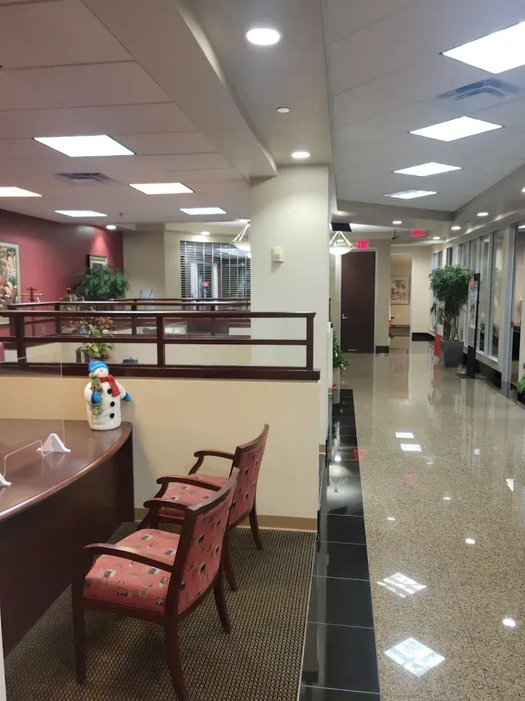 Office waiting area with chairs, desk, and hallway with doors. Shiny floor, recessed lighting.