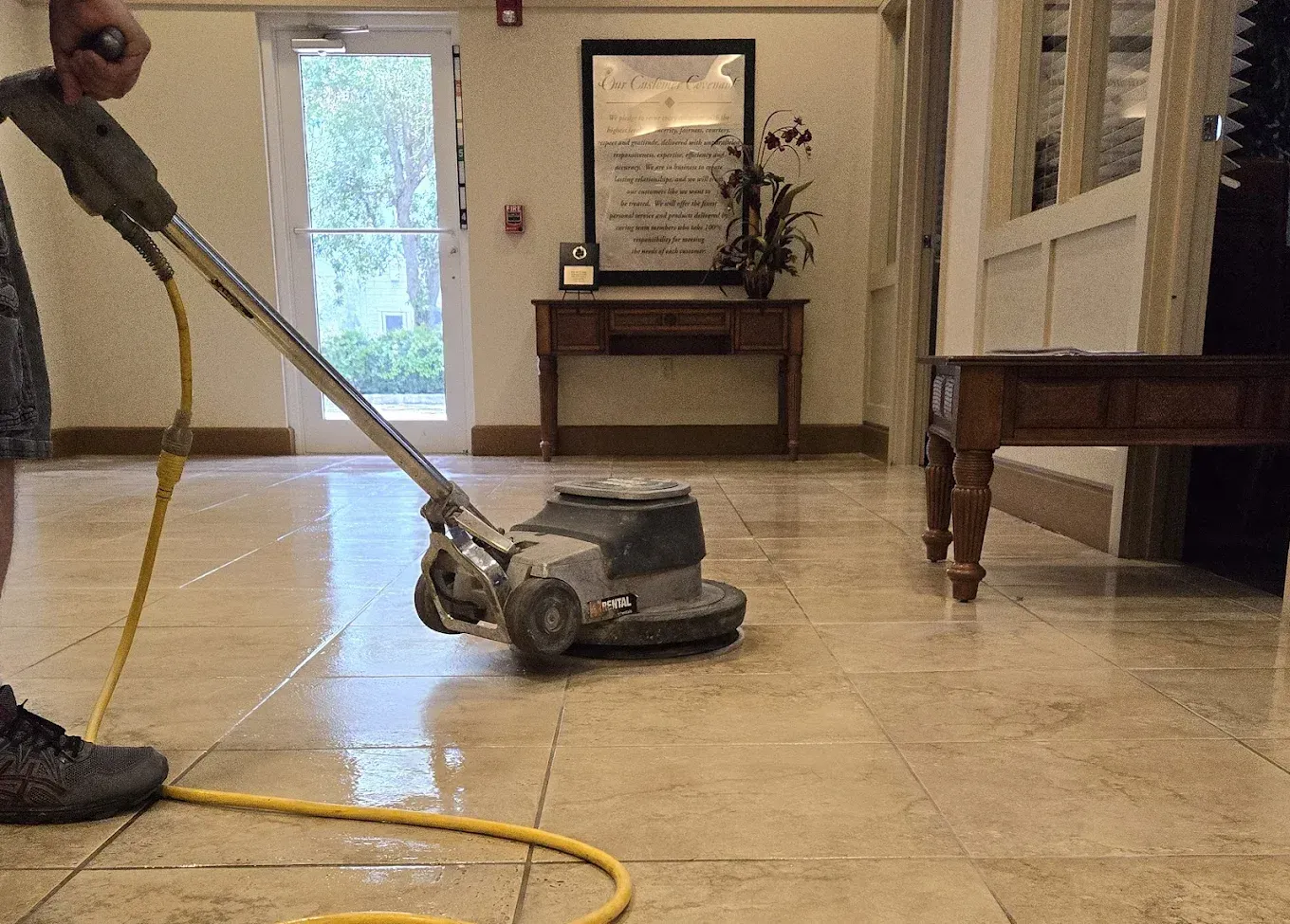 Person using a floor polishing machine on a tiled floor inside a building.