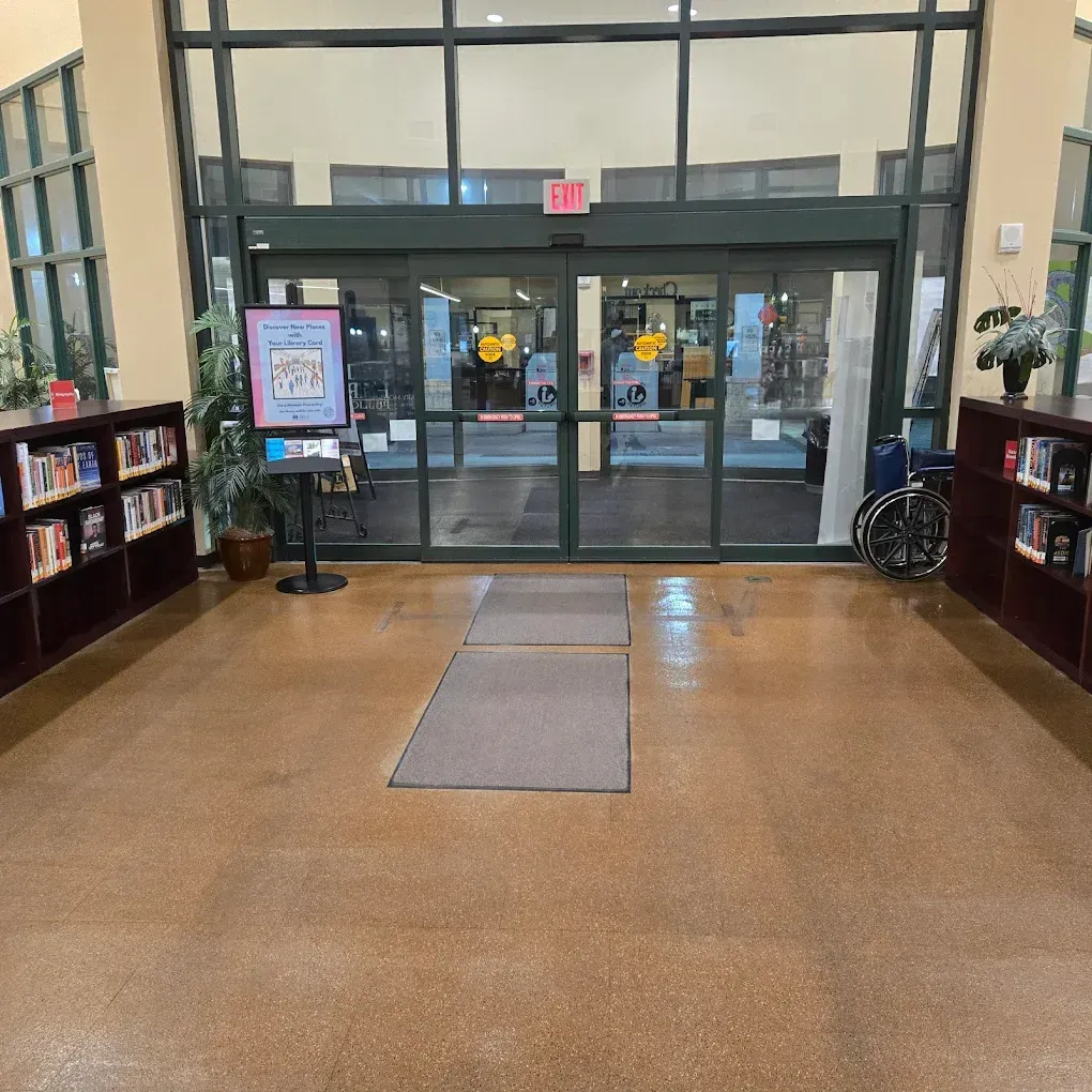 Entrance to a library with glass doors, bookshelves, a welcome sign, and a wheelchair.