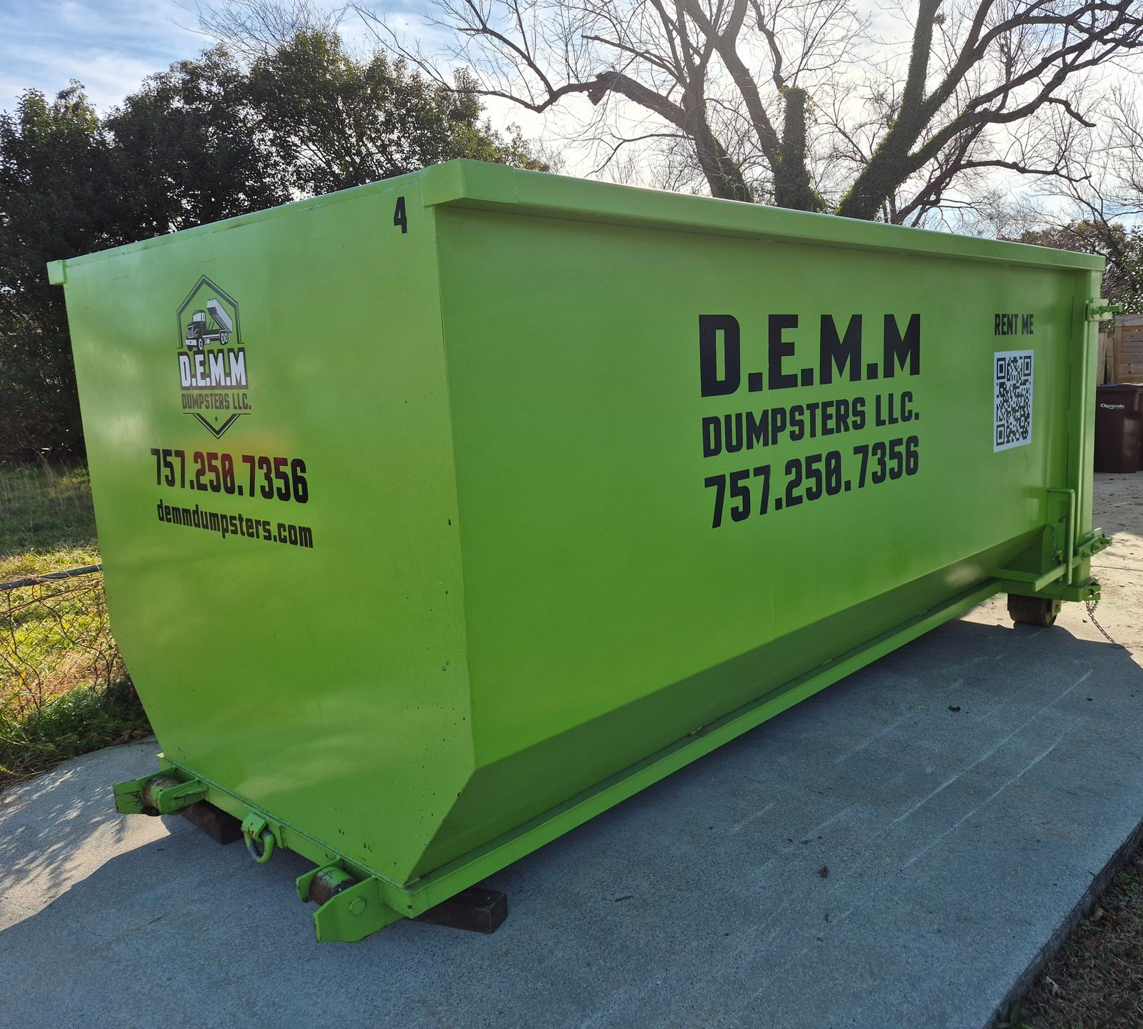 Two bright green industrial dumpsters sit outside, with lumber and pallets in the background.