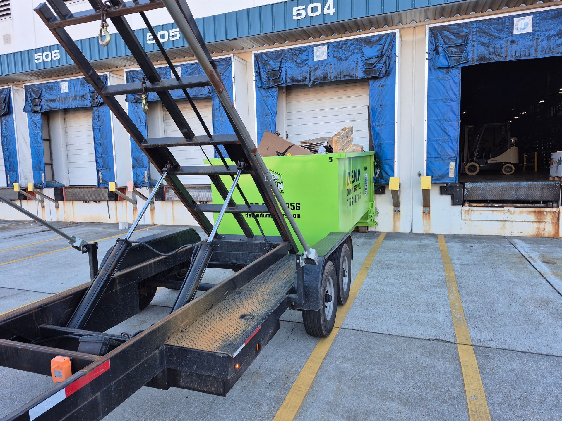 Green roll-off dumpster on a black trailer delivered to a Suffolk Virginia residential job