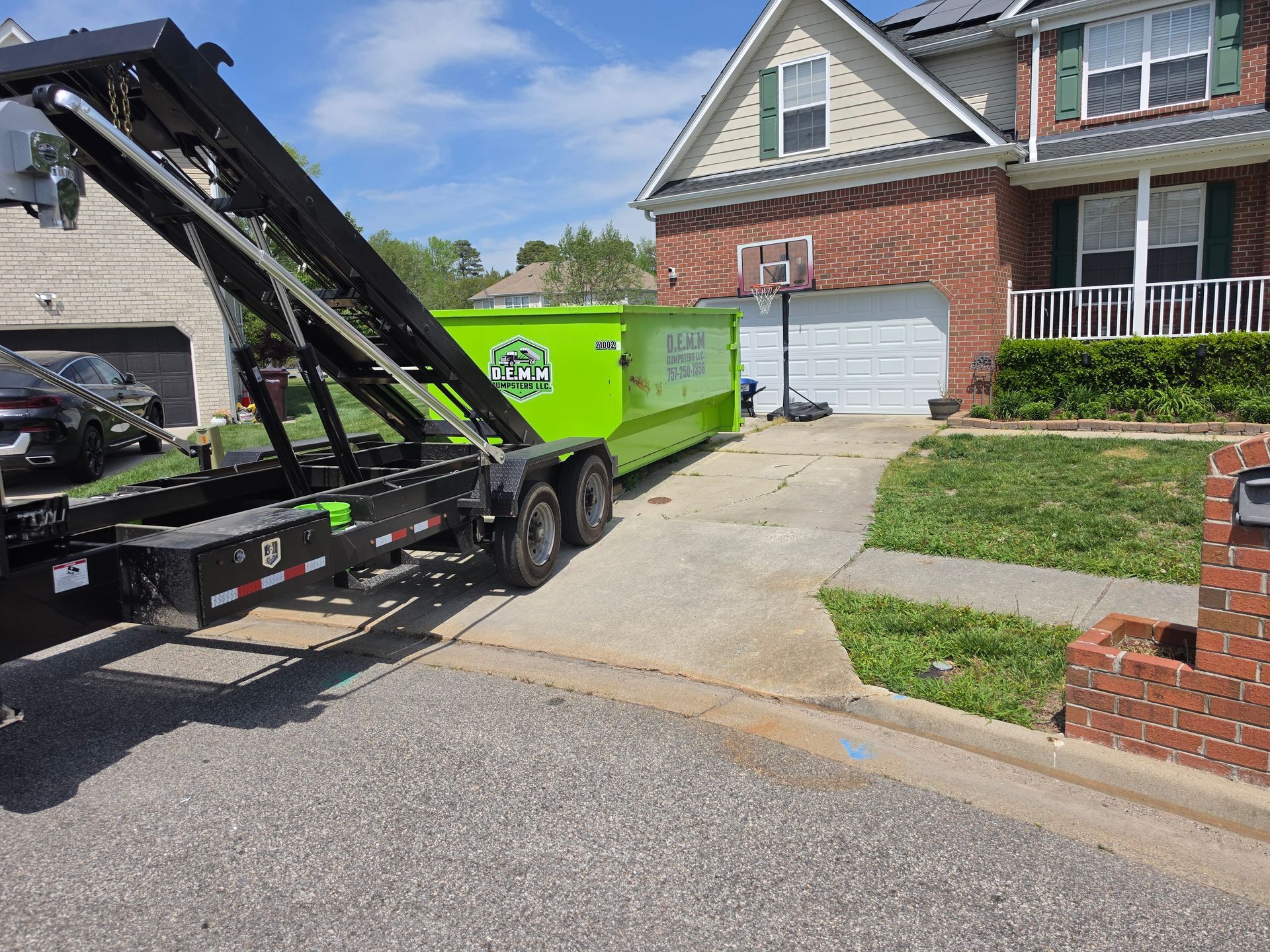 Black dumpster with overflowing debris sits outdoors in front of a brick building.
