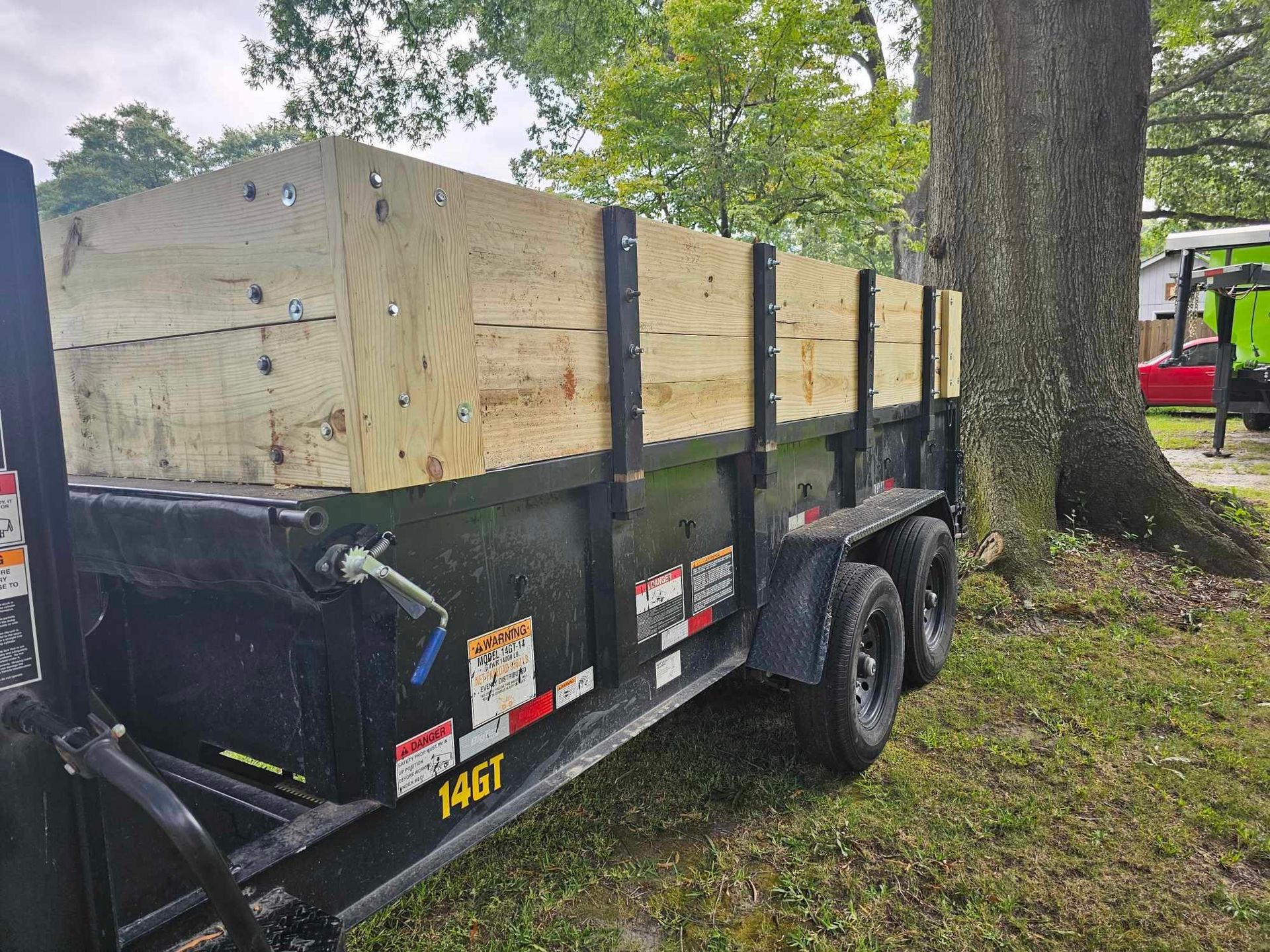 Bright green roll-off dumpster on a black trailer, parked on grass in a yard.