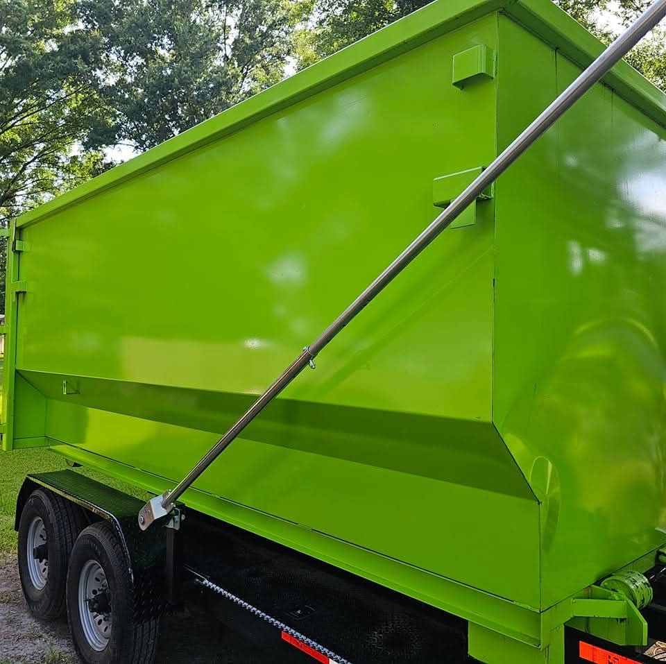 Bright green dumpster on a black trailer, outdoors. A long metal rod supports the lid.