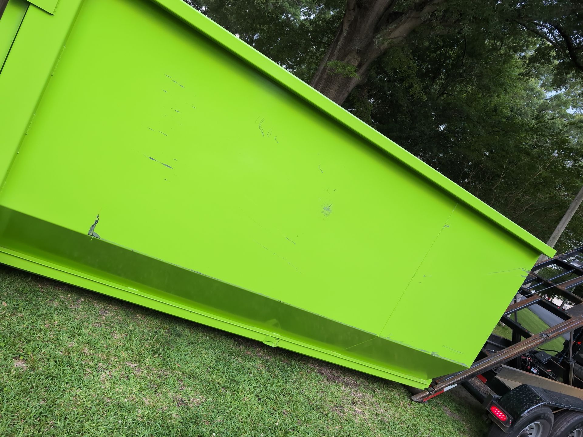 A bright green dumpster on a grassy lawn, angled, with a tree in the background.