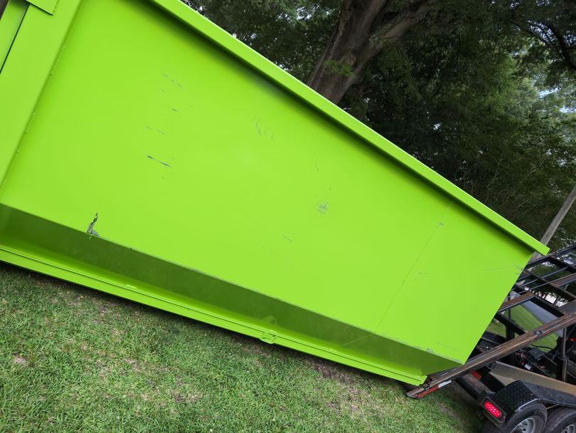 Lime green dumpster on grass, angled towards the viewer. Parts of a trailer are visible in the background.