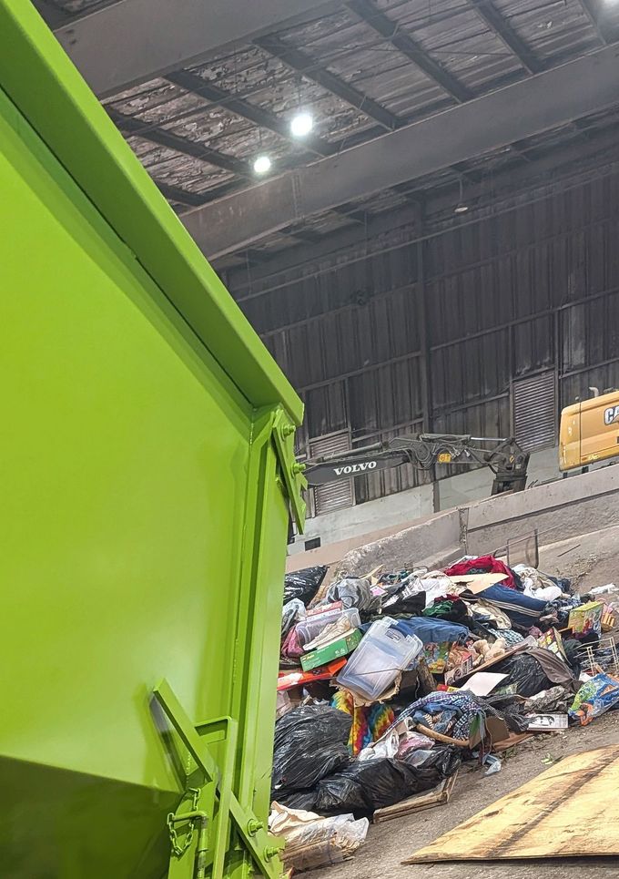 Green truck bed filled with textiles, likely for recycling, against a large industrial structure.