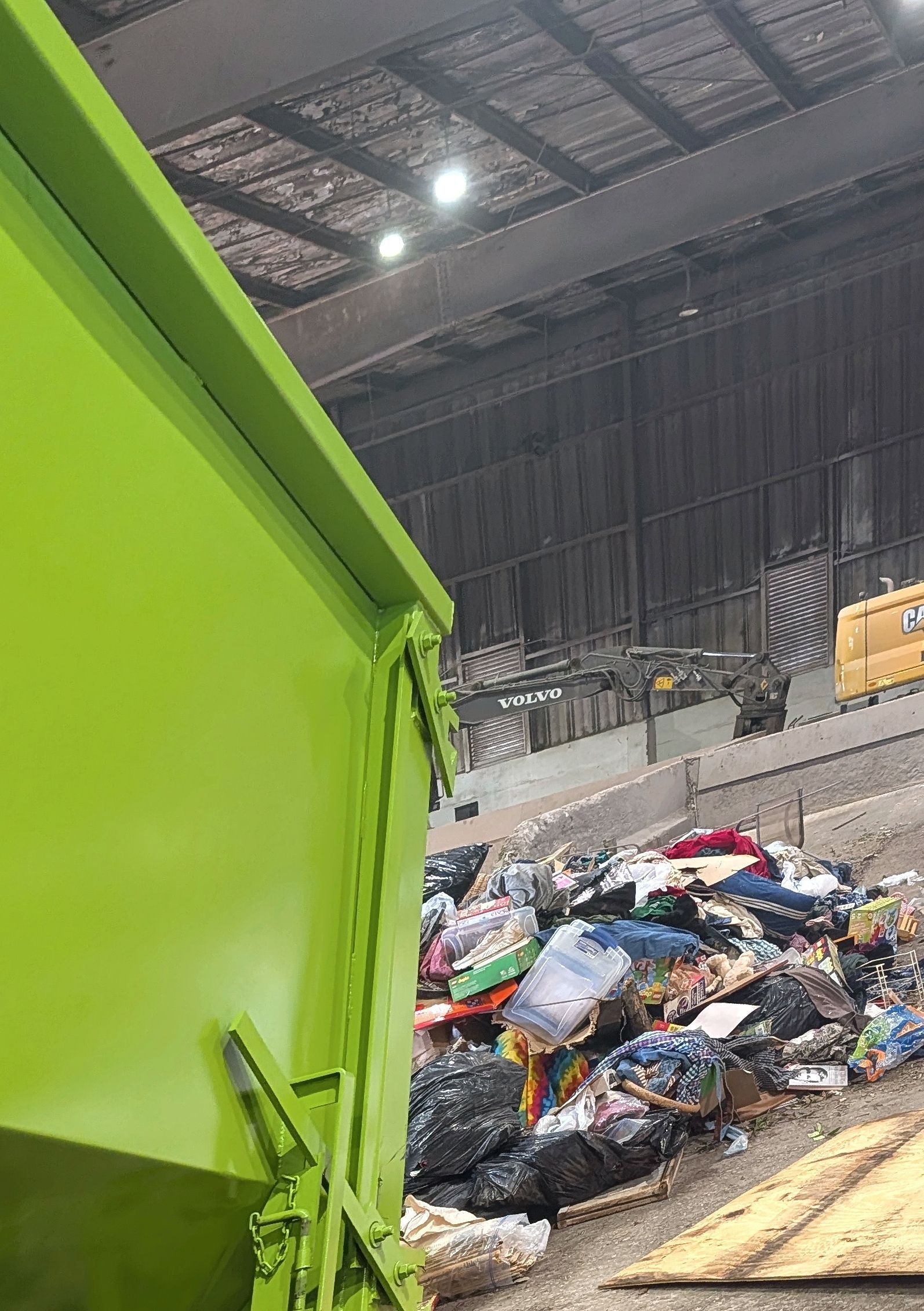 Green truck dumping textiles into a pile inside a recycling facility.