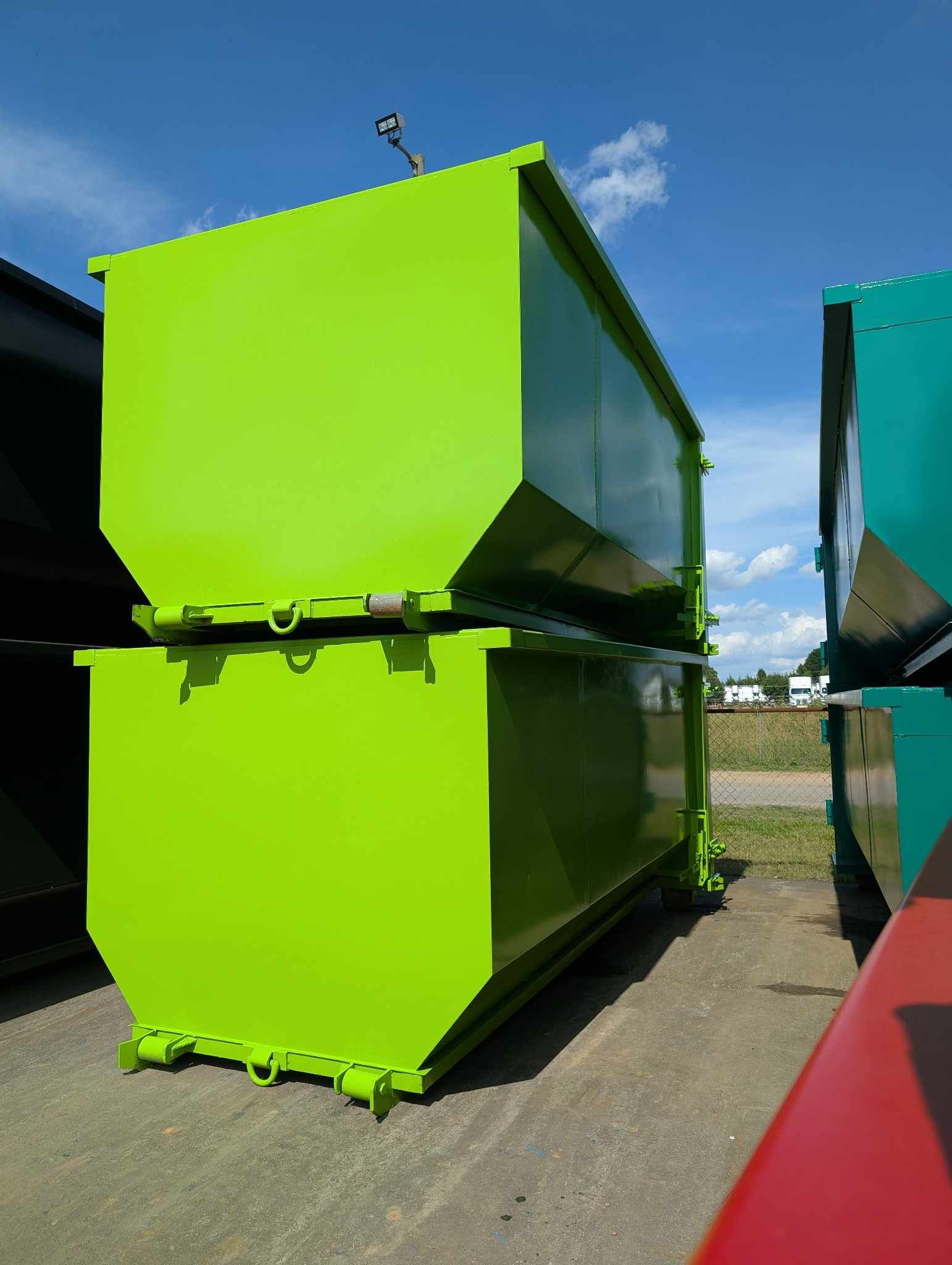 Two stacked, bright green industrial dumpsters under a blue sky.