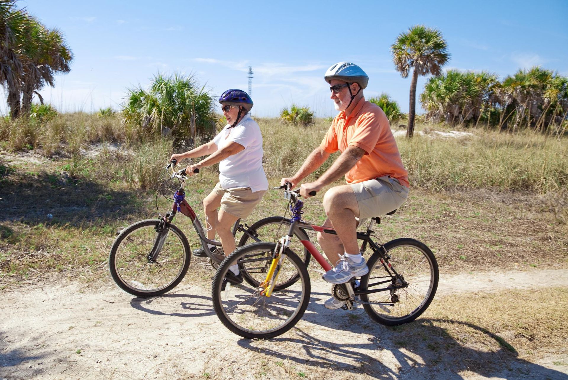 senior couple riding bicycles on beach path on a sunny day