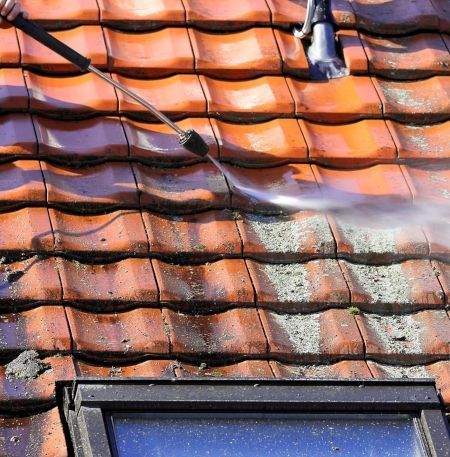 A person is cleaning a tiled roof in Bradford with a soft pressure washer.