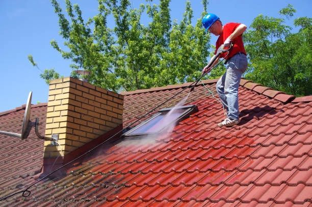 A man is cleaning a roof with a soft pressure washer. Bradford, UK.