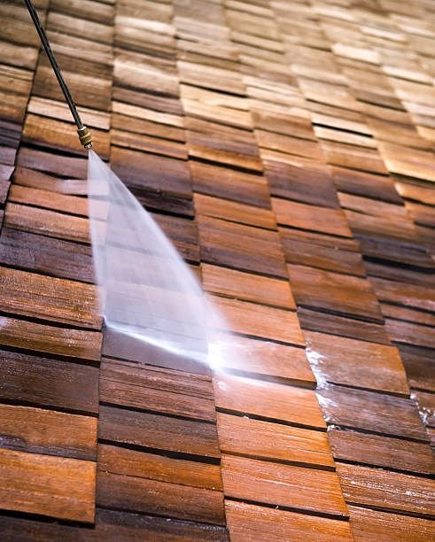 A person is cleaning moss from a tiled roof with a high pressure washer. Bradford, UK.