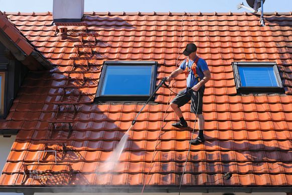 A man is cleaning moss from the roof of a house with a soft pressure washer. Bradford, UK.