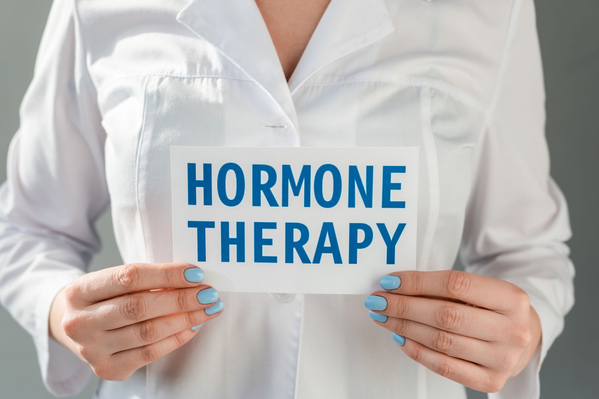 Person in lab coat holding a sign that reads 'Hormone Therapy' in bold blue letters.