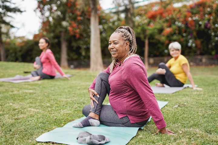 A group of women are sitting on yoga mats in a park