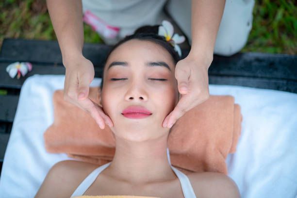 A woman receives a facial massage while laying down, with flowers in her head.