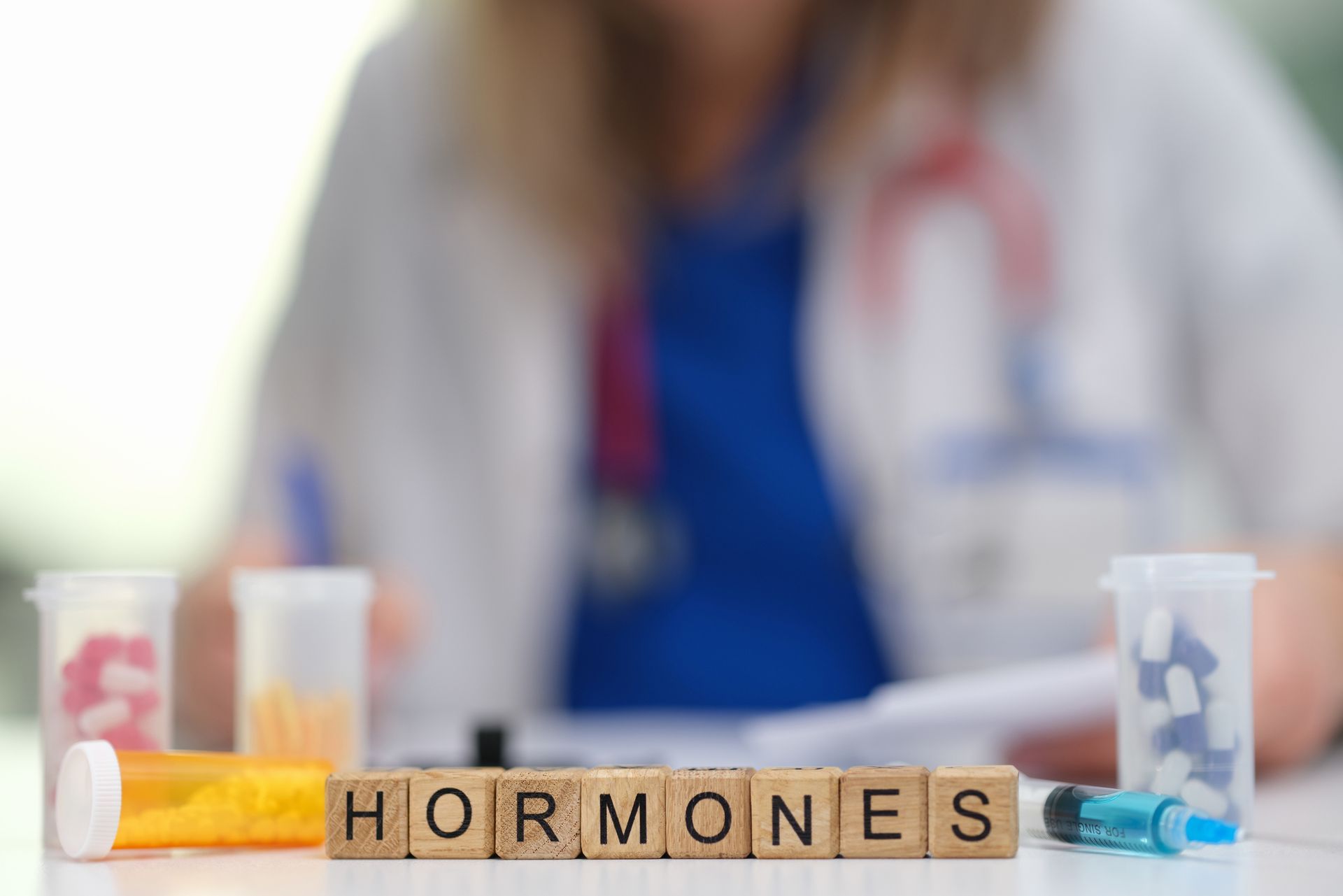 Wooden blocks spelling 'Hormones' with medical items and a doctor in the background. Wooden blocks spelling 'Hormones' with medical items and a doctor in the background.