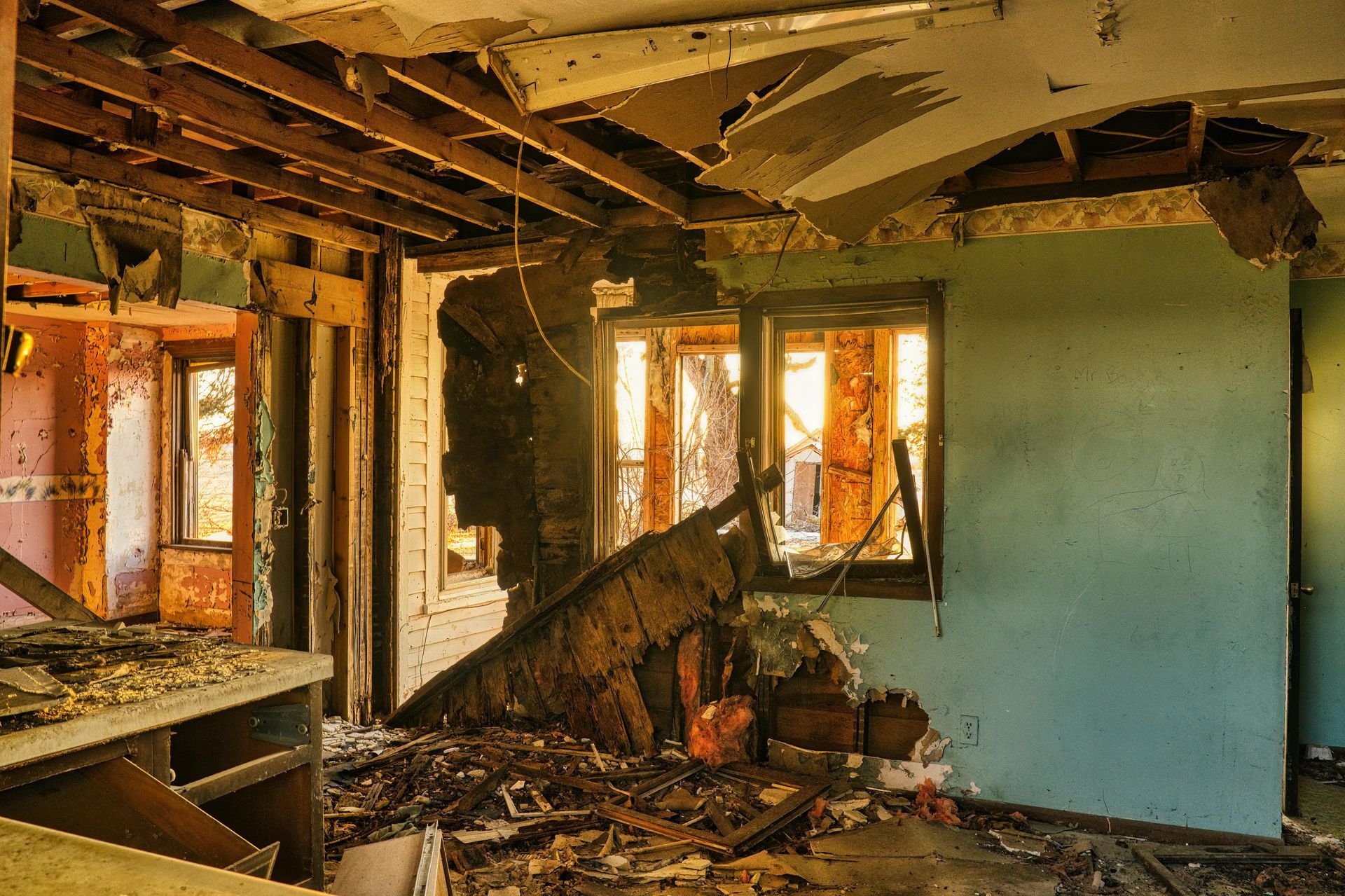 The interior of a derelict, fire-damaged room with exposed wooden ceiling beams and debris covering the floor.