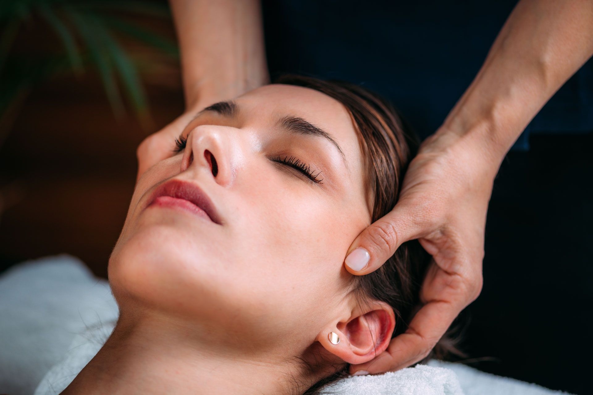 A person receiving a relaxing head massage with eyes closed, lying down on a white towel.