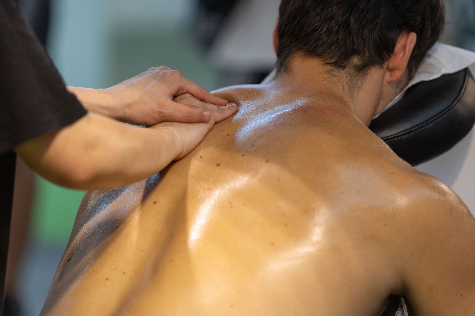 A person receives a back massage, with hands pressing into oiled, bare skin while the recipient rests on a headrest.