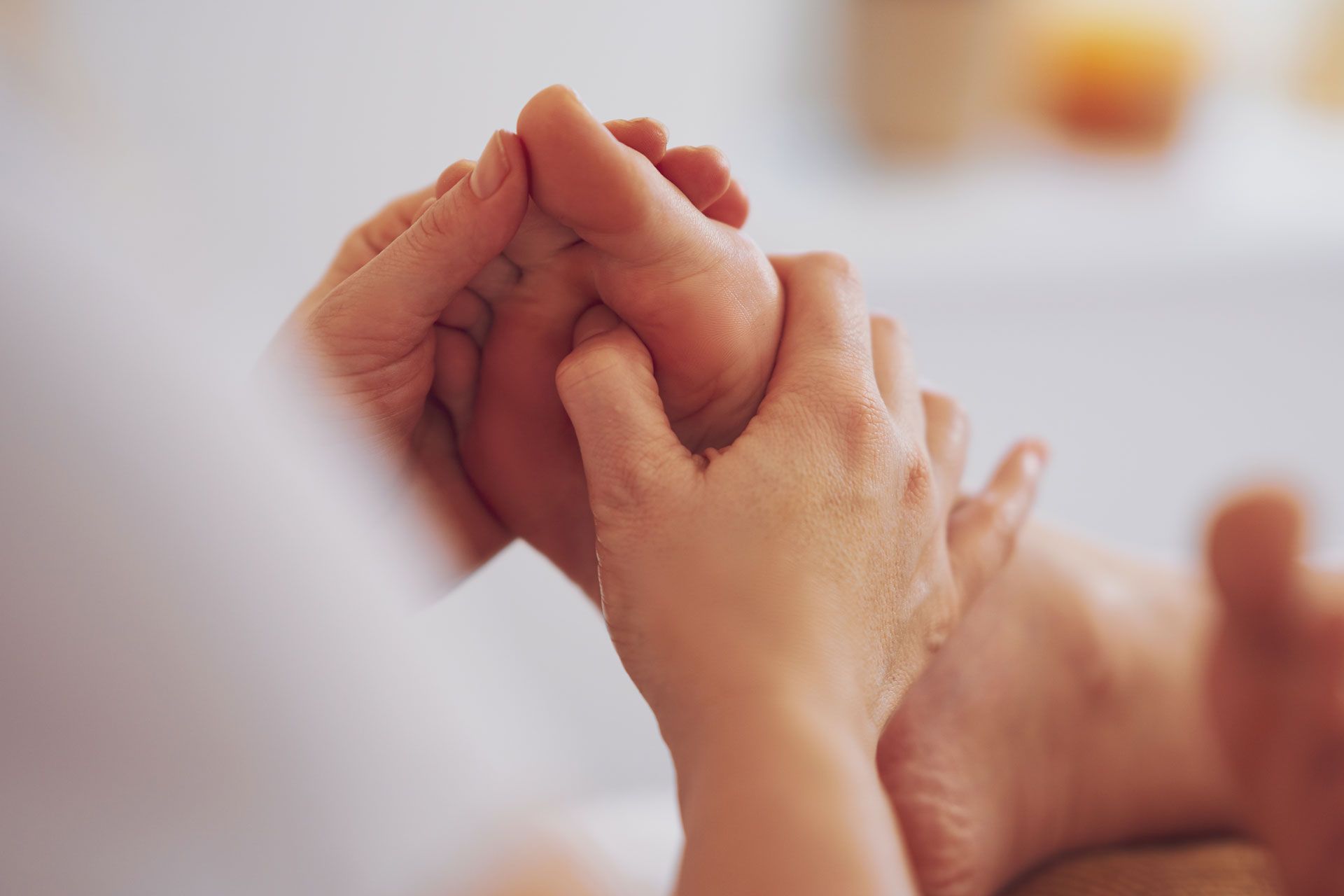 A close-up of a person's hands performing a foot massage, focusing on the sole of the foot.