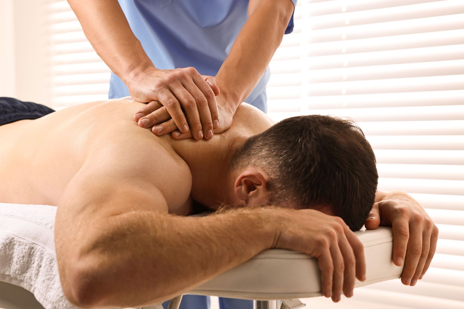 Medical professional giving a neck massage to a patient lying face down on a table; clinic setting.
