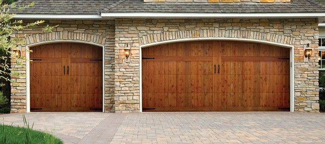 Two workers in red coveralls installing a white garage door in a building.