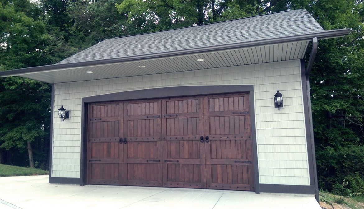 Driveway leading to open garage with tools and equipment inside. White building with green lawn.