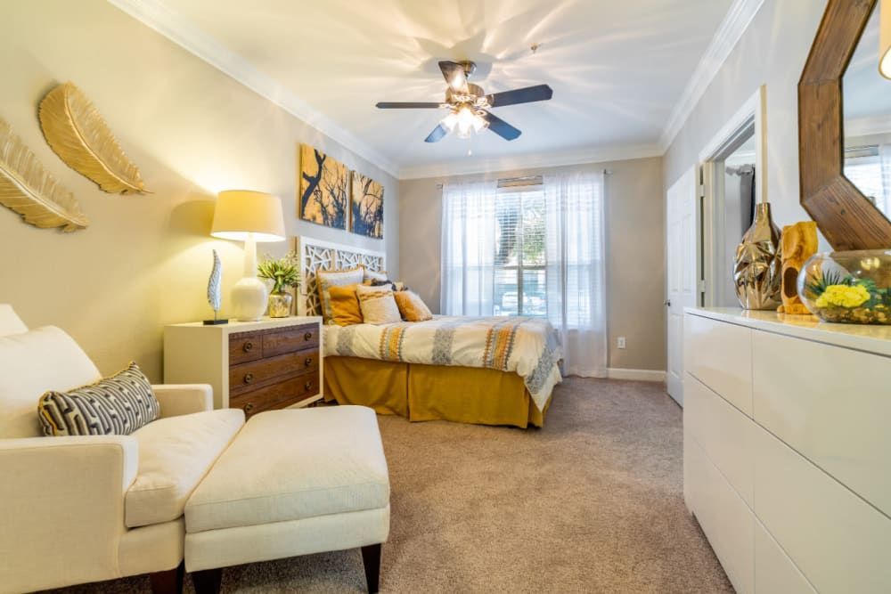 a bedroom with a bed, chair, ottoman, and ceiling fan at Marquis at Great Hills in Austin, TX.