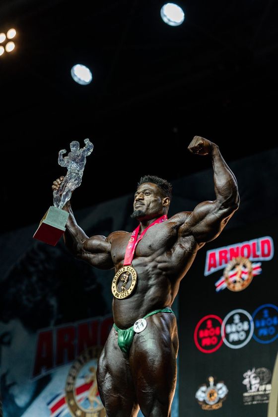 A very muscular man is holding a trophy in his hand.