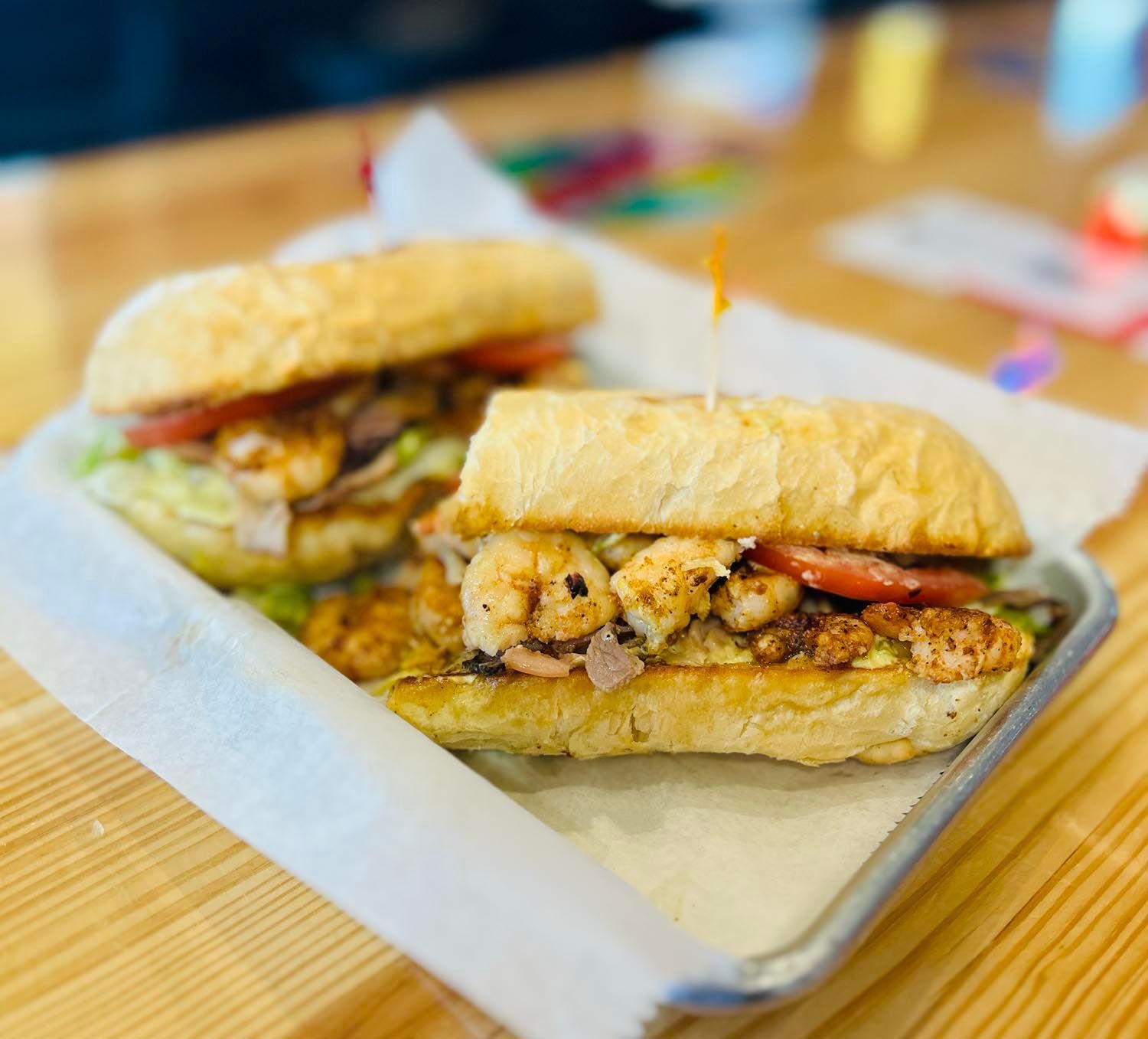 Two shrimp sandwiches are sitting on a metal tray on a wooden table.