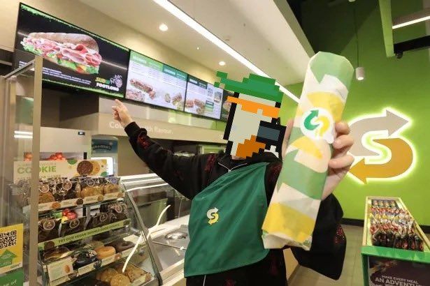 A person is holding a subway sandwich in a store.