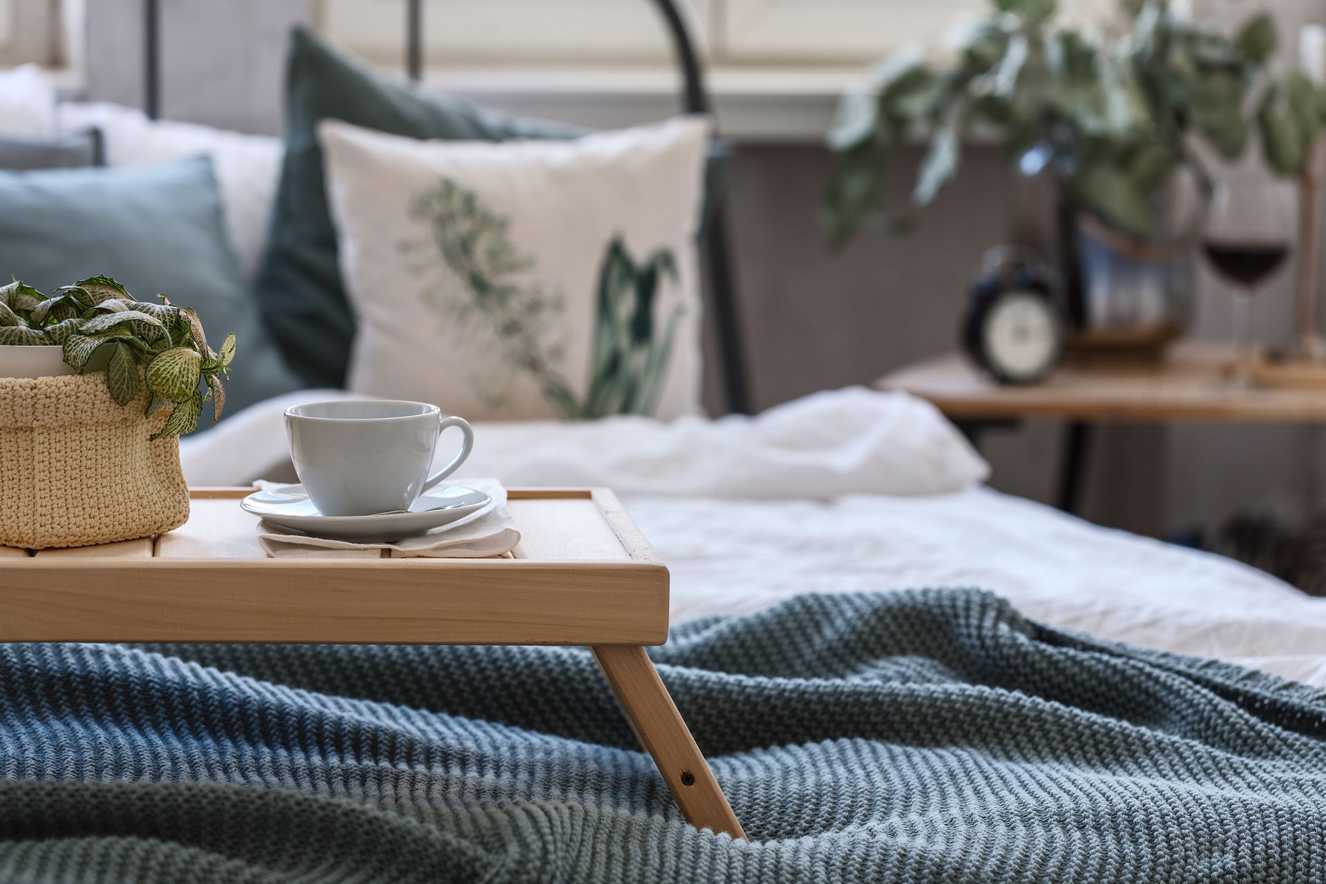 A wooden tray with a cup of coffee on it is sitting on top of a bed .