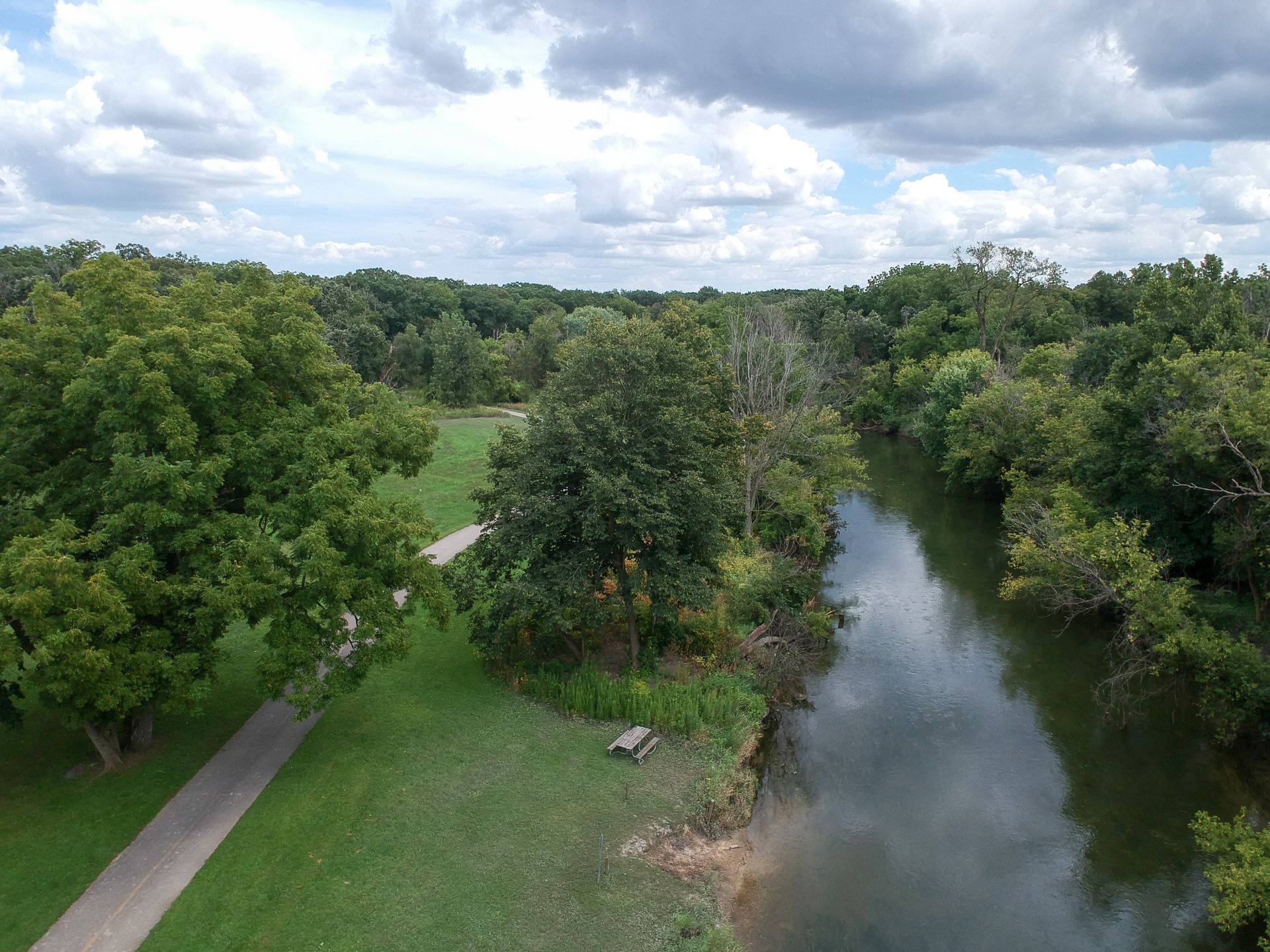 River flowing through a park with trees and a paved path under a cloudy sky.