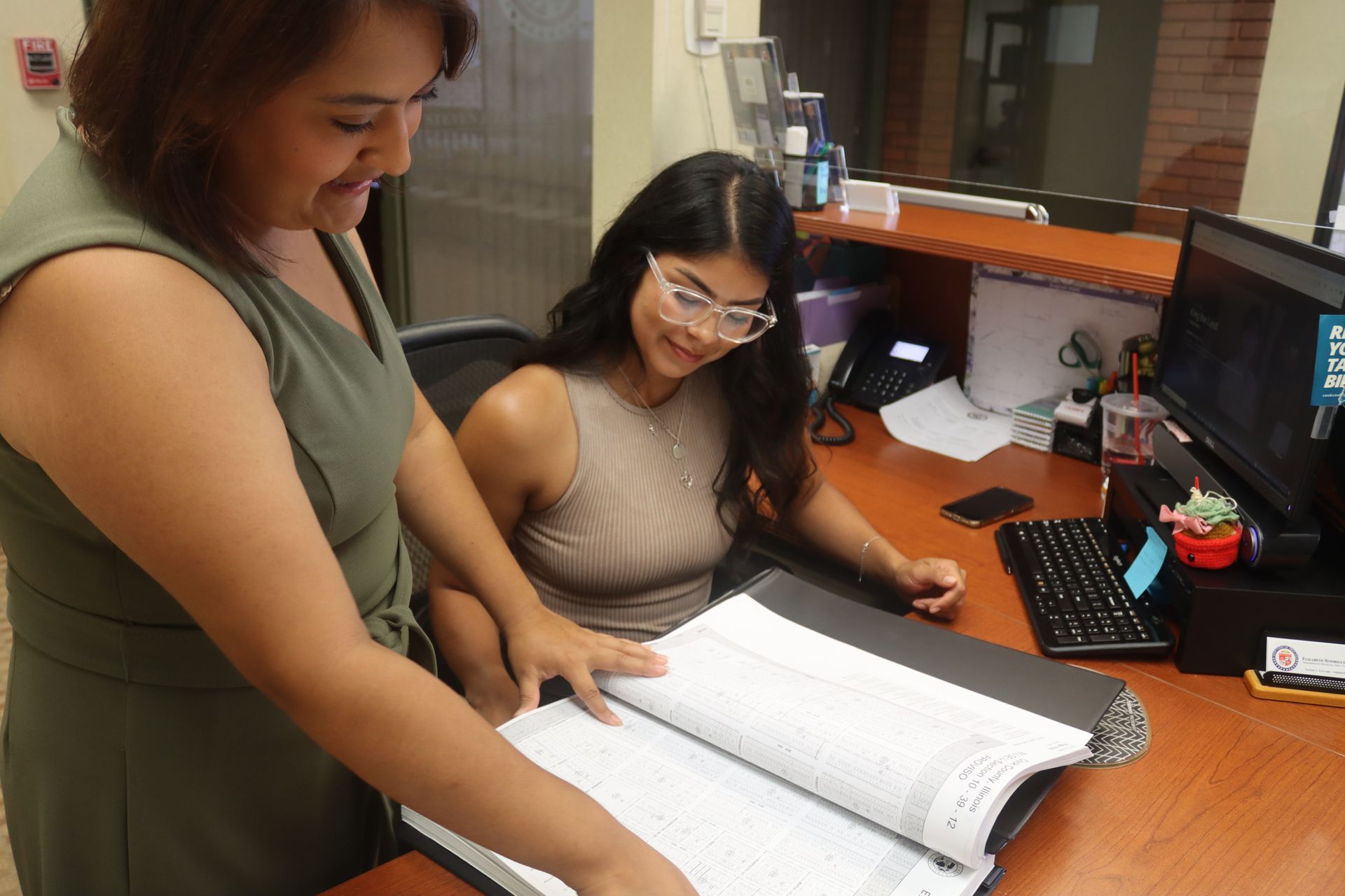 Two women looking at a large open book at a desk in an office. One points to the book.