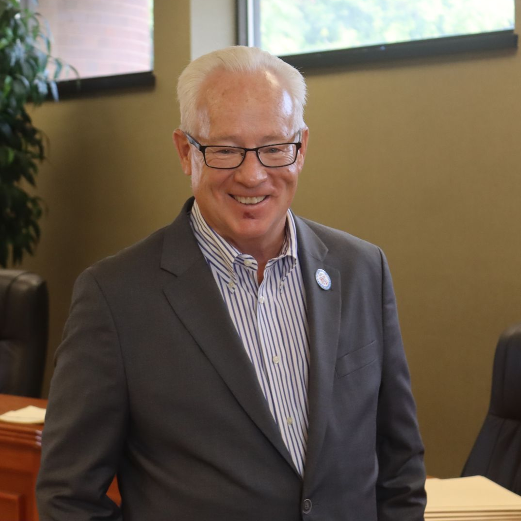 Man wearing glasses and a suit, smiling in an office setting.