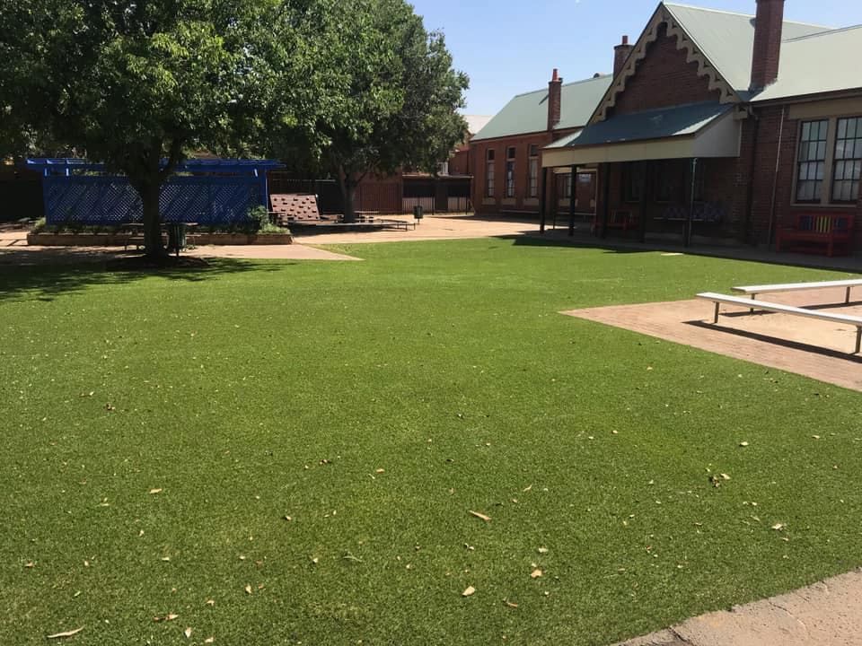 Lush Green Artificial Turf in a Schoolyard, Brick Building — Dubbo Premier Landscapes in Dubbo, NSW