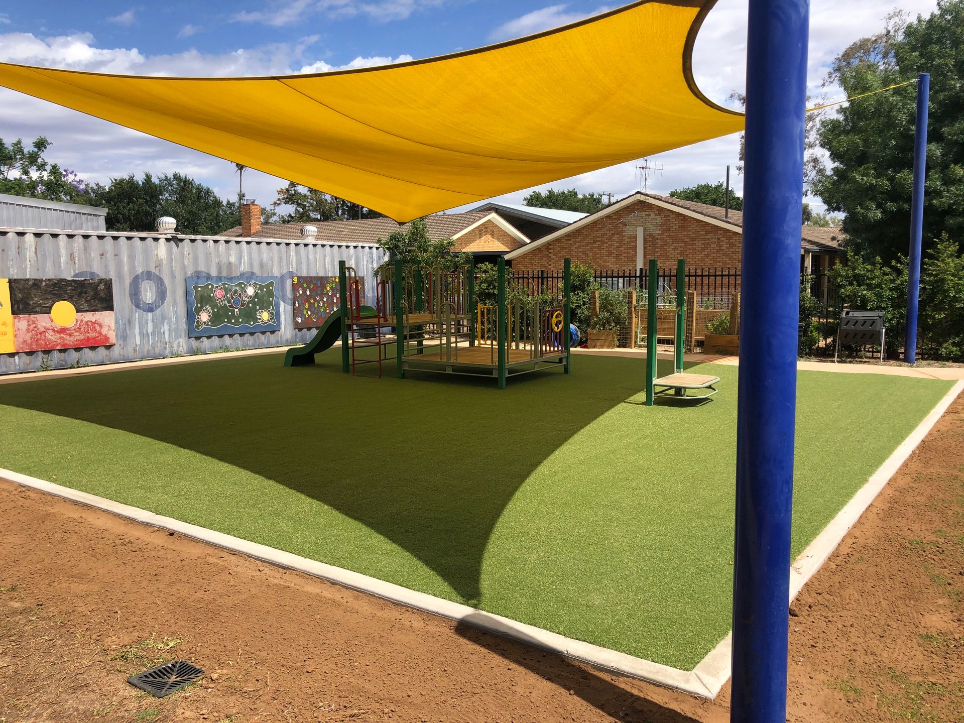 Playground with yellow shade sail, green turf and play equipment — Dubbo Premier Landscapes in Dubbo, NSW