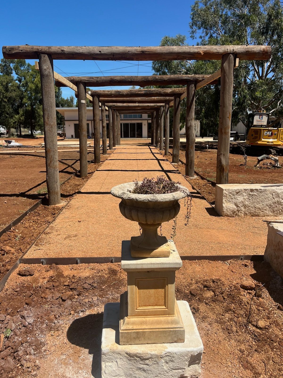 Stone urn on a pedestal in a garden pathway lined with wooden pergola frames— Dubbo Premier Landscapes in Dubbo, NSW