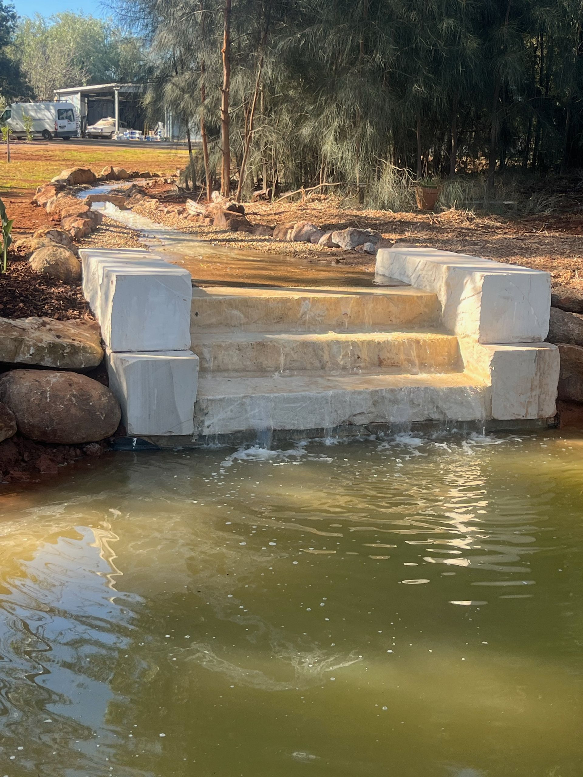 Concrete steps leading into a pond, surrounded by rocks and dirt — Dubbo Premier Landscapes in Dubbo, NSW