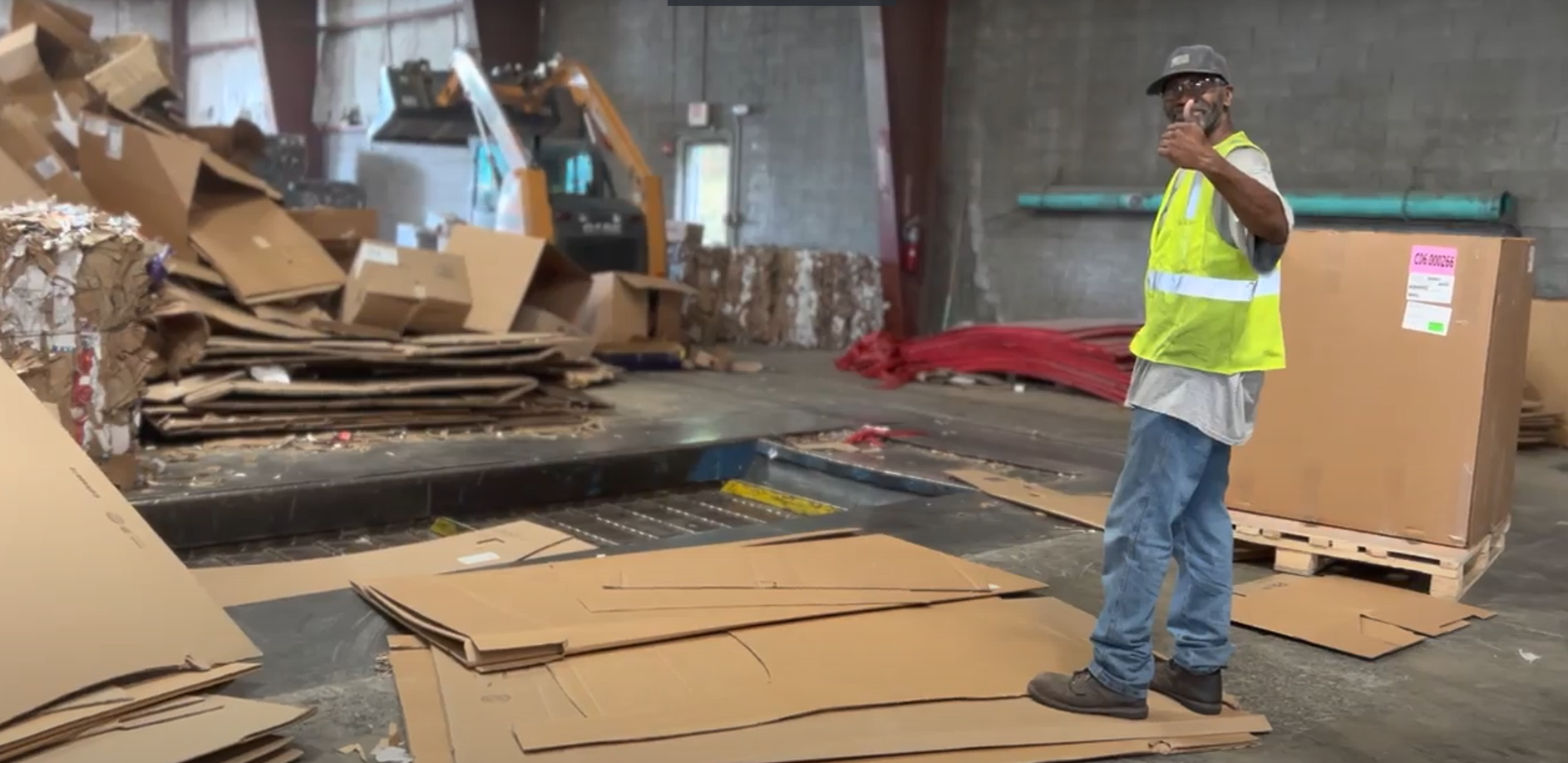 A man in a yellow vest is standing in a room filled with cardboard boxes.