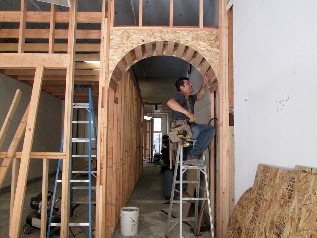 A man on a ladder is working on a wooden archway