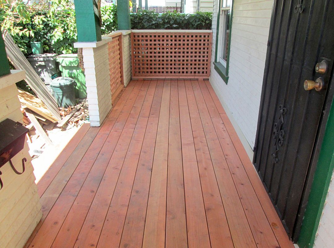 A porch with a wooden floor and a green door