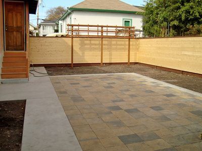 A backyard with a wooden fence and a brick walkway